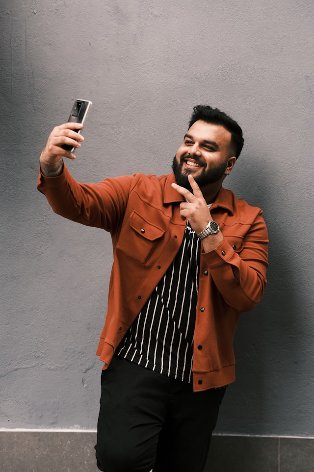 Um homem a sorrir enquanto filma um vídeo de si próprio com o telemóvel.