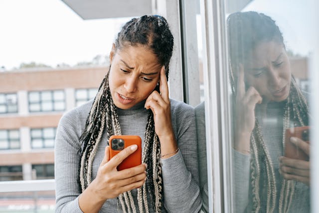 Uma mulher aflita a olhar para o telemóvel enquanto esfrega a têmpora com o dedo.