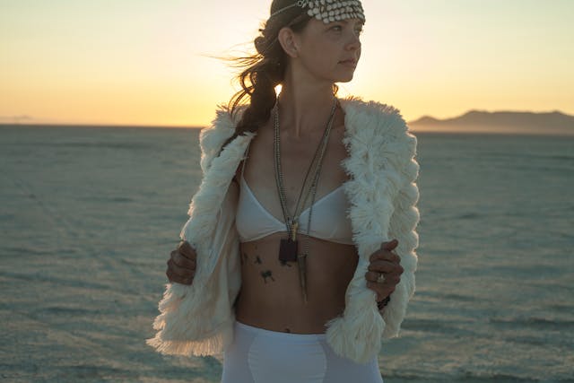 Uma mulher tatuada com um casaco de pele branco e acessórios boémios.