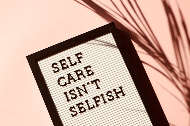 Um quadro a preto e branco com a frase "Cuidar de si próprio não é egoísmo" sobre um fundo cor-de-rosa