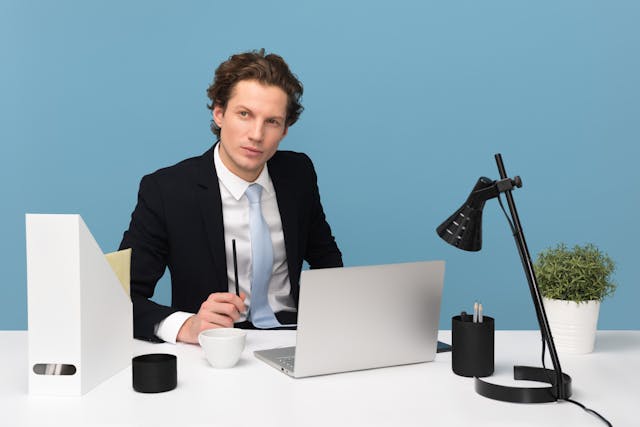 Un uomo d'affari seduto sulla scrivania del suo ufficio con un computer portatile, una lampada e altri oggetti essenziali per l'ufficio.