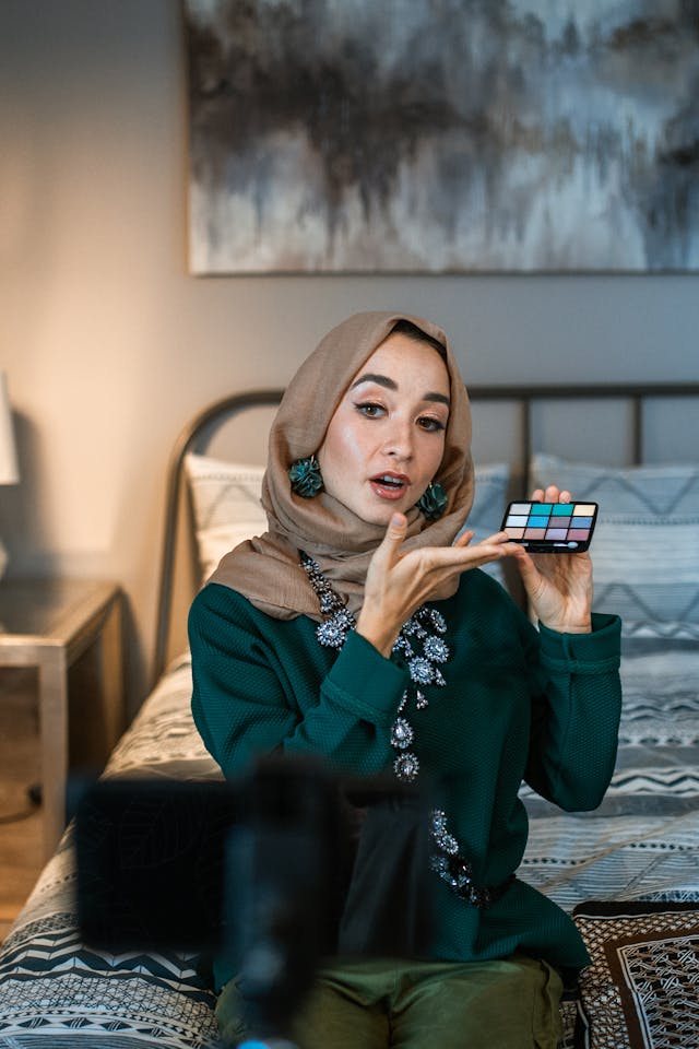 A female influencer filming a product review while holding up a makeup palette.