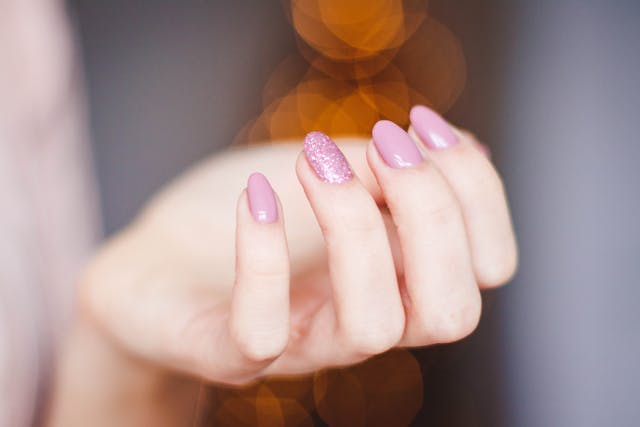 Die Hand einer Frau mit einer hellrosa Maniküre mit Glitter auf nur einem Nagel.