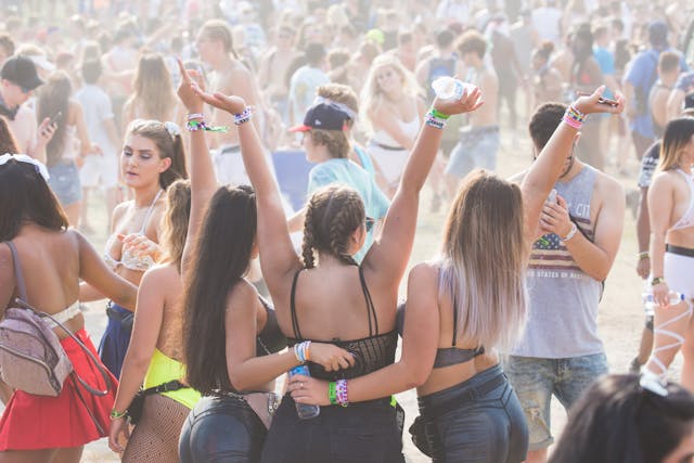 Um homem tira uma fotografia a três raparigas num festival cheio de gente.