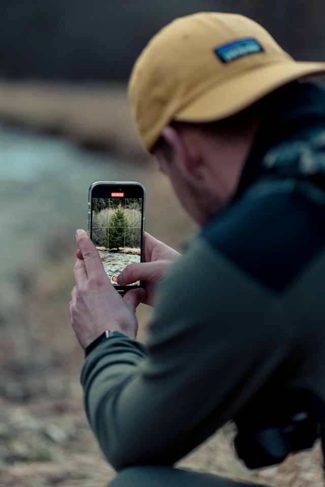 Um homem filma um vídeo de um rio e de árvores com o seu smartphone.