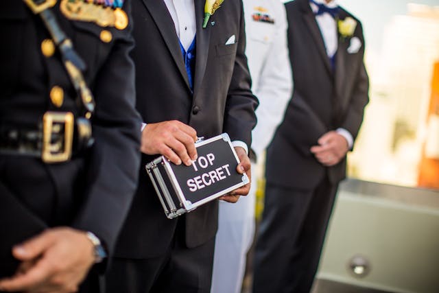 A man wearing a suit in line with other men while holding a briefcase with the words “TOP SECRET” on it.