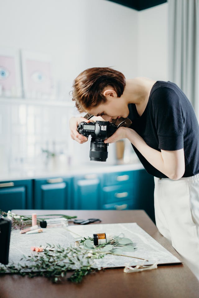 A female content creator taking a flat-lay photo of flowers and skincare products with a professional camera.