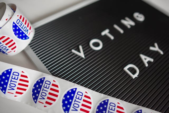 Un letrero que dice "Voting Day" junto a rollos de pegatinas con la bandera estadounidense que dicen "Voted".