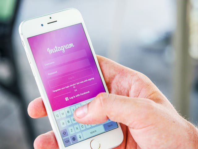 O persoană ține în mână un iPhone alb cu pagina de logare roz Instagram pe ecran.