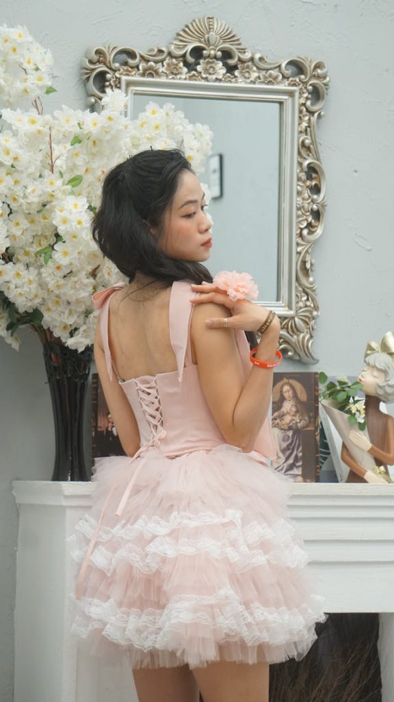A young woman wearing a pink, corseted mini dress with a skirt layered with plenty of feminine ruffles.