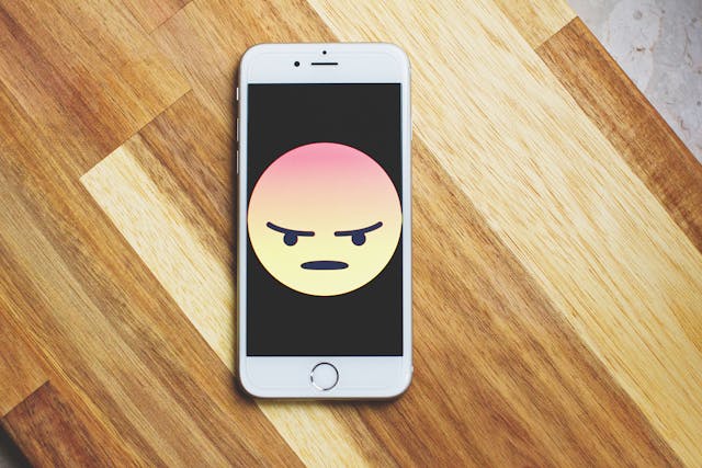 Un iPhone plateado con un emoji enfadado en la pantalla.