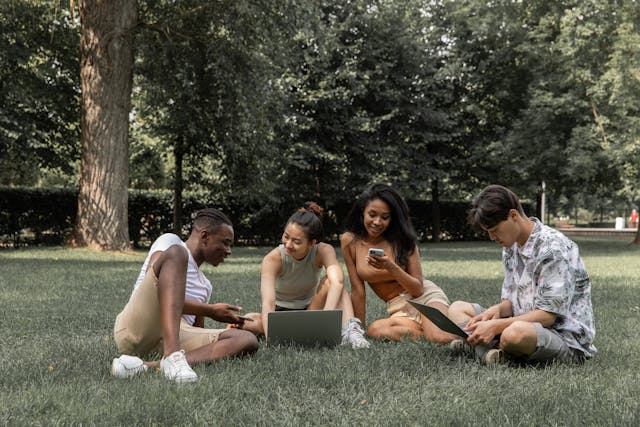 Um grupo de amigos no parque, todos a olhar para uma conversa de grupo através dos seus respectivos dispositivos.