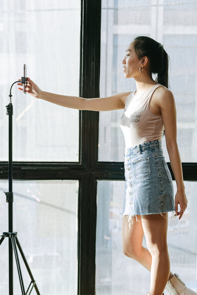 O femeie creatoare de conținut își ajustează telefonul pe un trepied pentru a filma un videoclip cu ea însăși.