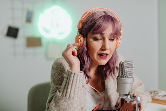  Uma influenciadora com cabelo cor-de-rosa a usar auscultadores e a falar para um microfone para gravar um podcast.