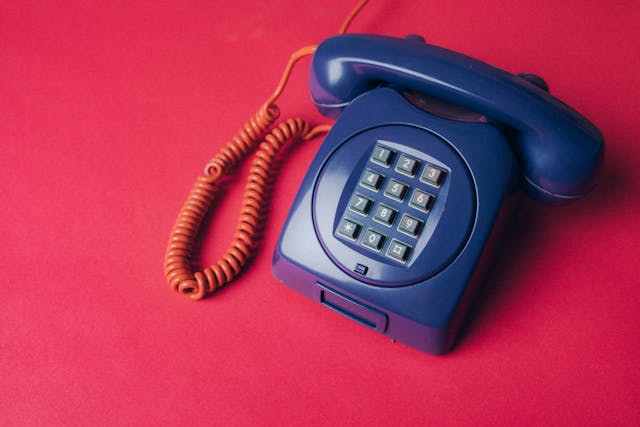 Um telefone com fios azul-marinho da velha guarda numa superfície vermelha.