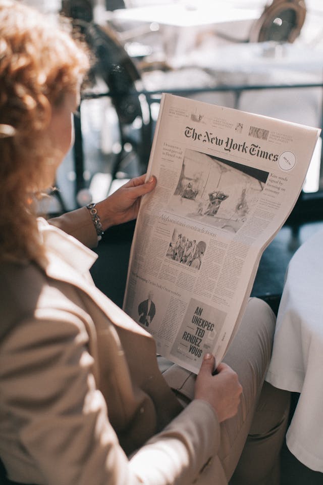A woman reading the front page of the New York Times newspaper.