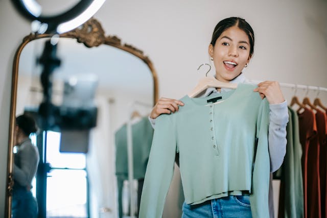 Eine glückliche Inhaltserstellerin nimmt ein Video auf, in dem sie einen Pullover einer Modemarke hochhält.