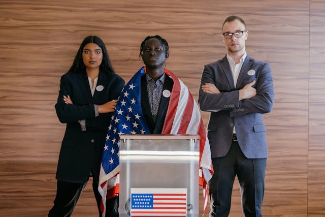Um adolescente num pódio com a bandeira americana aos ombros, enquanto dois outros jovens estão atrás dele.
