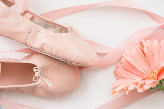 A pair of pink ballet flats next to a pink flower.