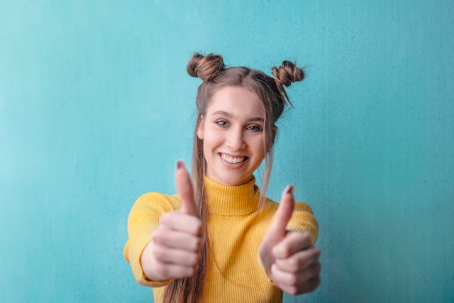 黄色いセーターを着た女性が笑顔で親指を2本立てている。