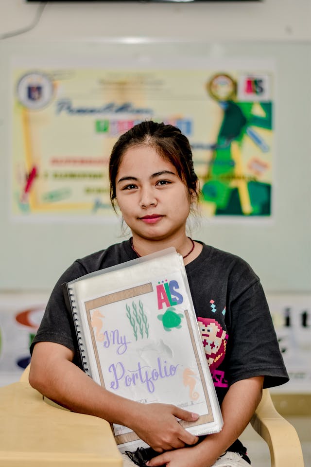 Una mujer joven sostiene una carpeta de exposición que dice "mi portafolio" en la portada.