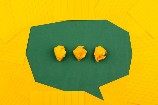 Papéis amarelos, lisos e amarrotados, dispostos numa superfície verde para criar a silhueta de um ícone DM.