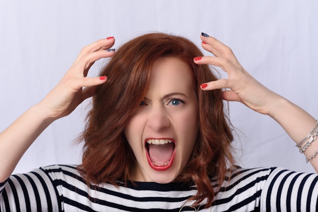 Uma mulher frustrada a gritar enquanto levanta as mãos acima da cabeça com raiva.